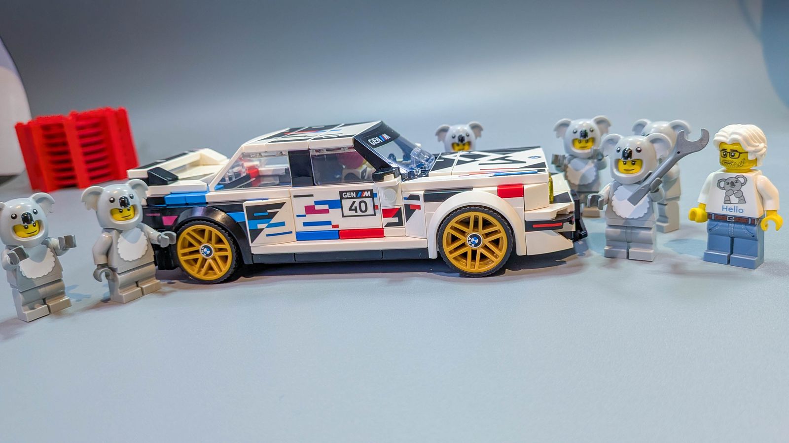 The finished LEGO BMW M3 E30 in side profile, surrounded by the koala minifigure crew