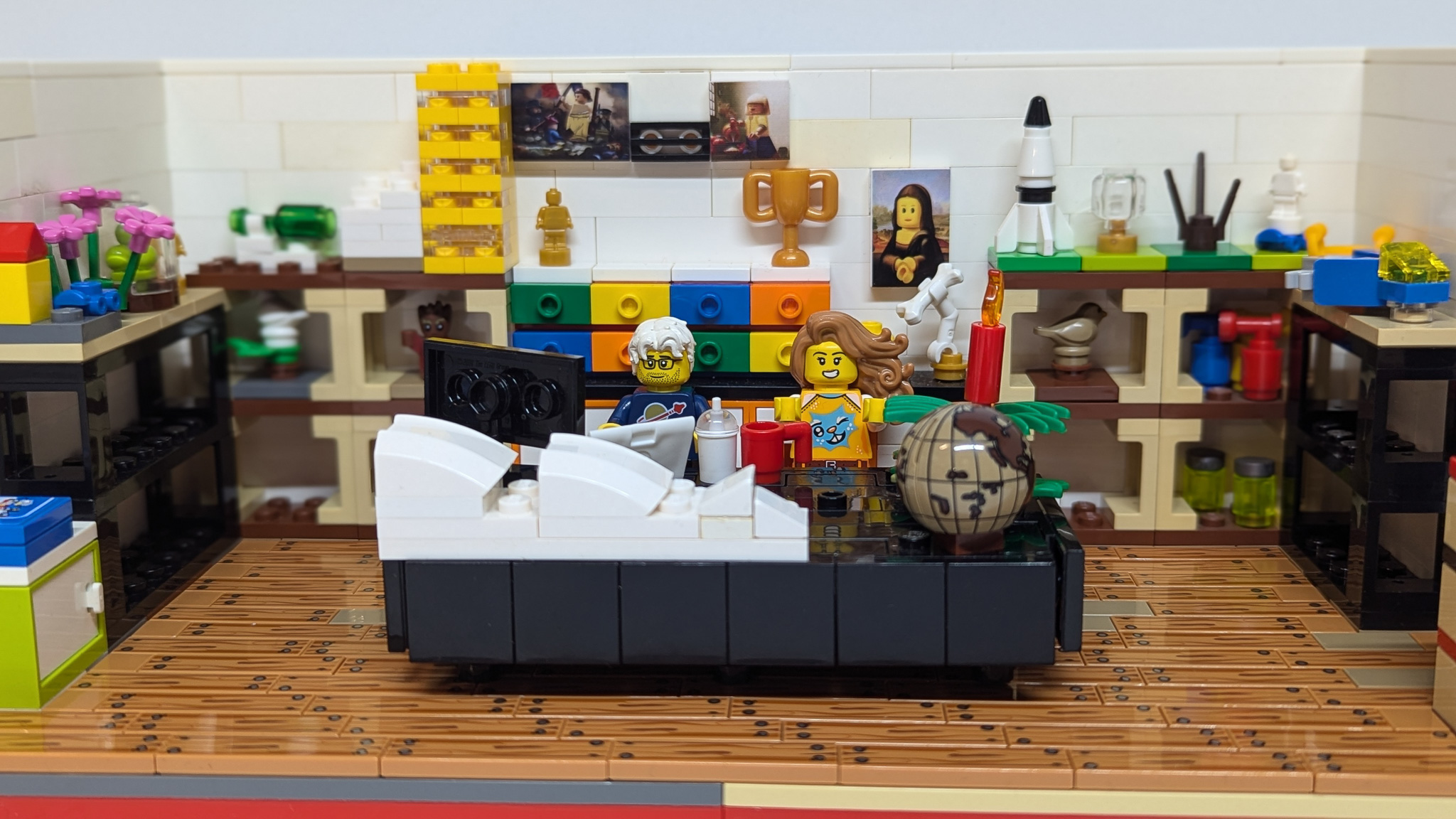 A minifigure-scale LEGO room with shelves, colourful drawers and two minifigures on a couch